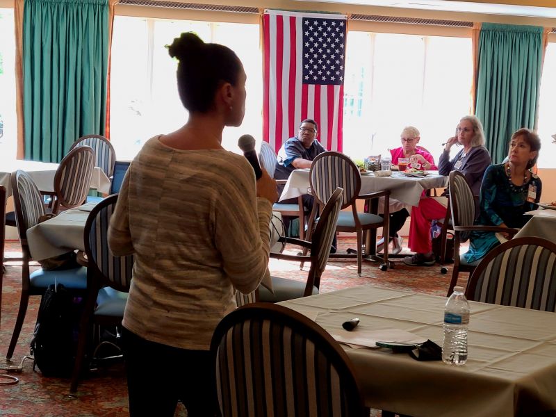 Woman speaking to a group of adults through a microphone
