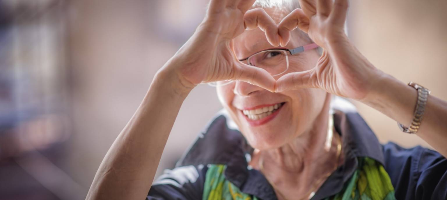 charming older lady smiling and making a heart with her hands